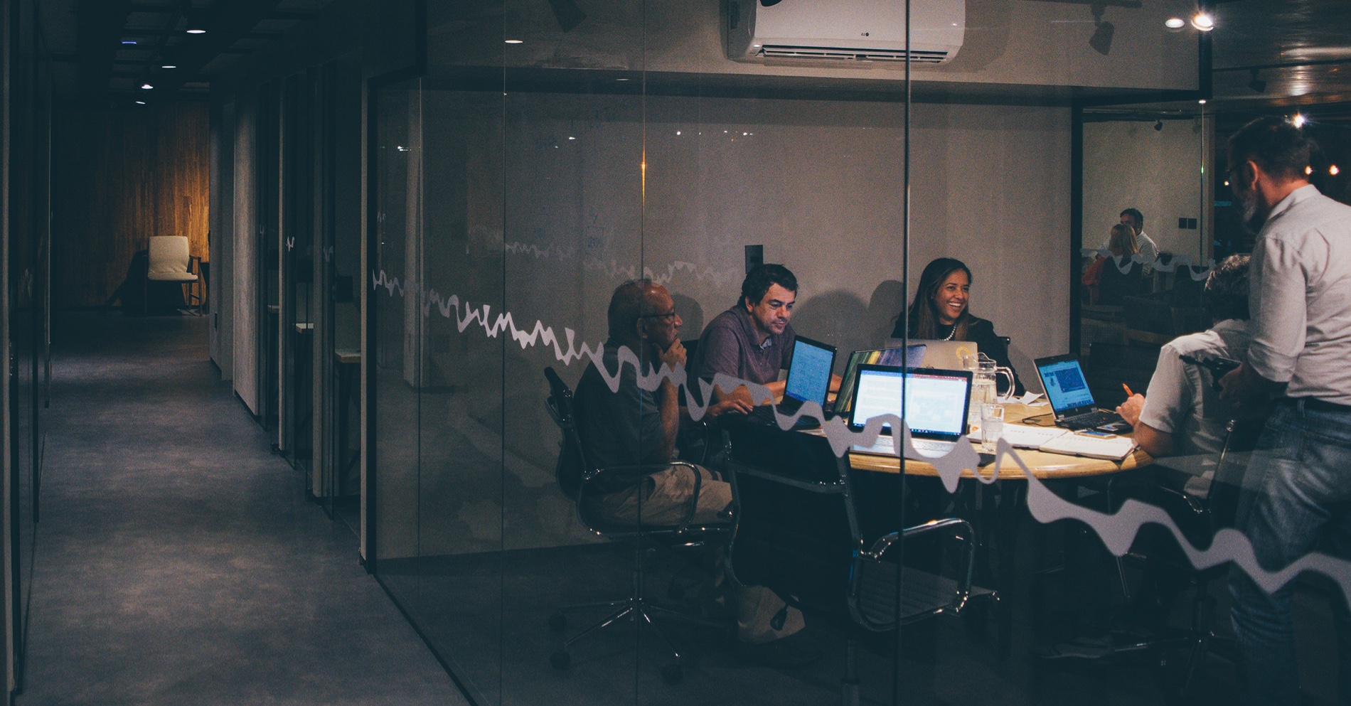 A group of people in a business meeting, behind the glass of an office.